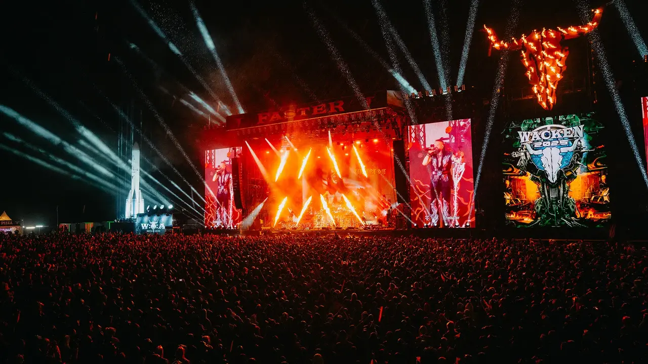 Large crowd at a music festival with bright stage lights and visual displays, featuring a prominent bull sculpture above the stage.