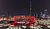 Coca-Cola Arena illuminated at night, featuring a modern design with red accents, surrounded by Dubai's skyline and skyscrapers.
