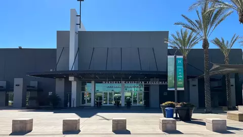Entrance of Harvest Christian Fellowship featuring a cross, palm trees, and a large glass door with a welcoming sign.