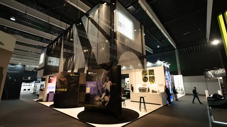 A modern exhibition booth featuring large displays, seating areas, and a sleek design, set in a spacious trade show environment.