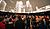 A crowd gathers in a venue with a large projection of city buildings on the ceiling, creating an immersive atmosphere for an event.