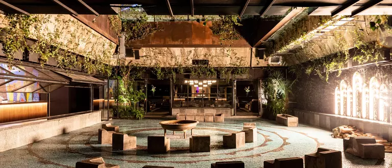 Modern indoor space featuring a circular arrangement of stone seating, surrounded by greenery and illuminated by ambient lighting.