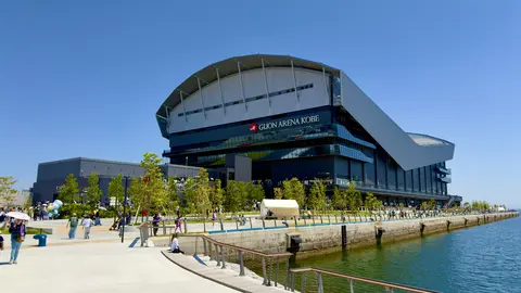 Gugon Arena in Korea, a modern architectural structure, surrounded by greenery and a waterfront promenade, with people walking nearby.