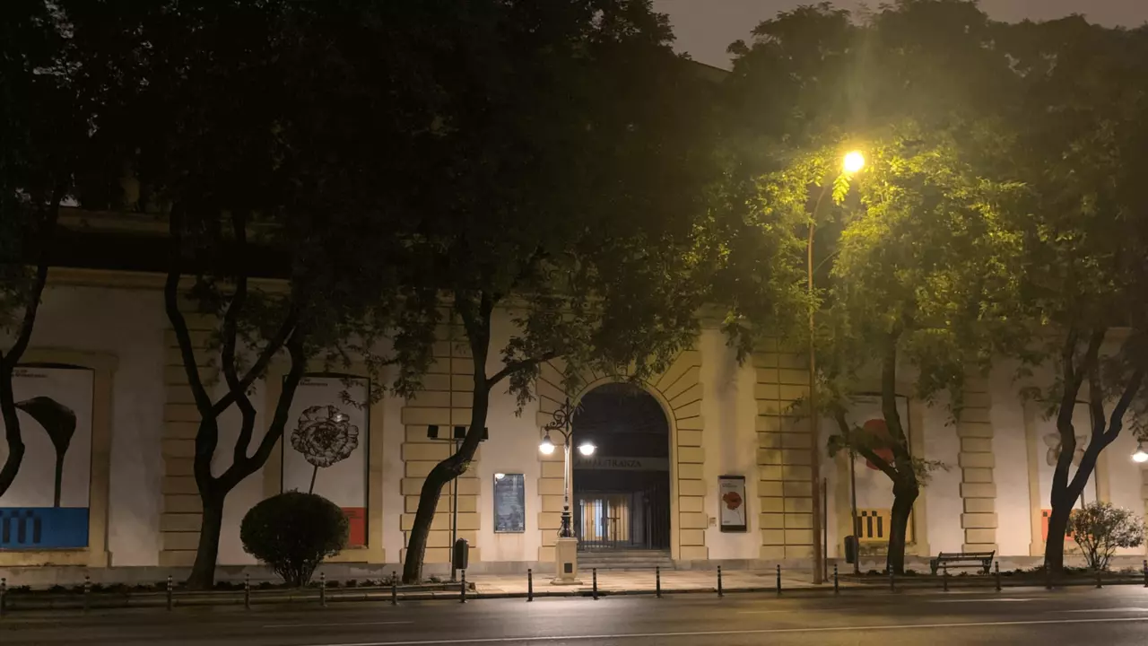 Historic building entrance illuminated by streetlights, surrounded by trees, with posters visible on the walls.