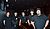 Five individuals in black shirts stand together in a dimly lit venue, smiling and posing for the camera.