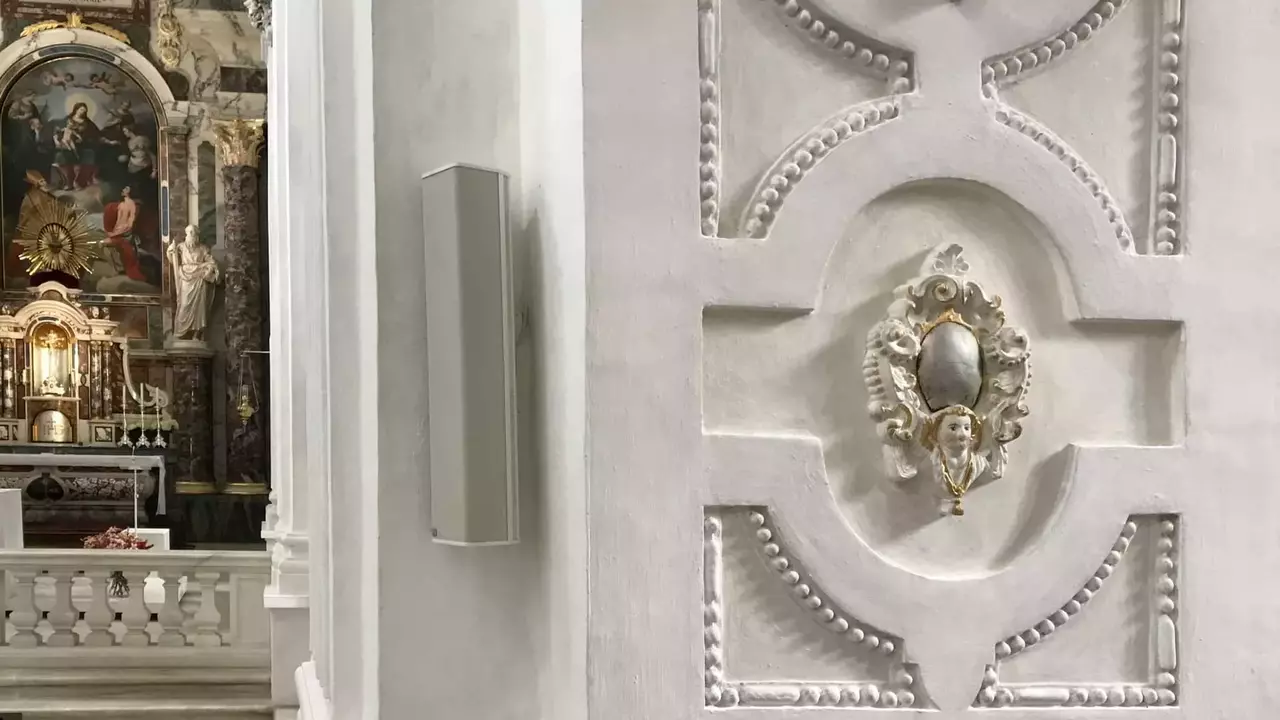 Ornate wall detail featuring decorative molding and a central medallion, with a glimpse of an altar in the background.