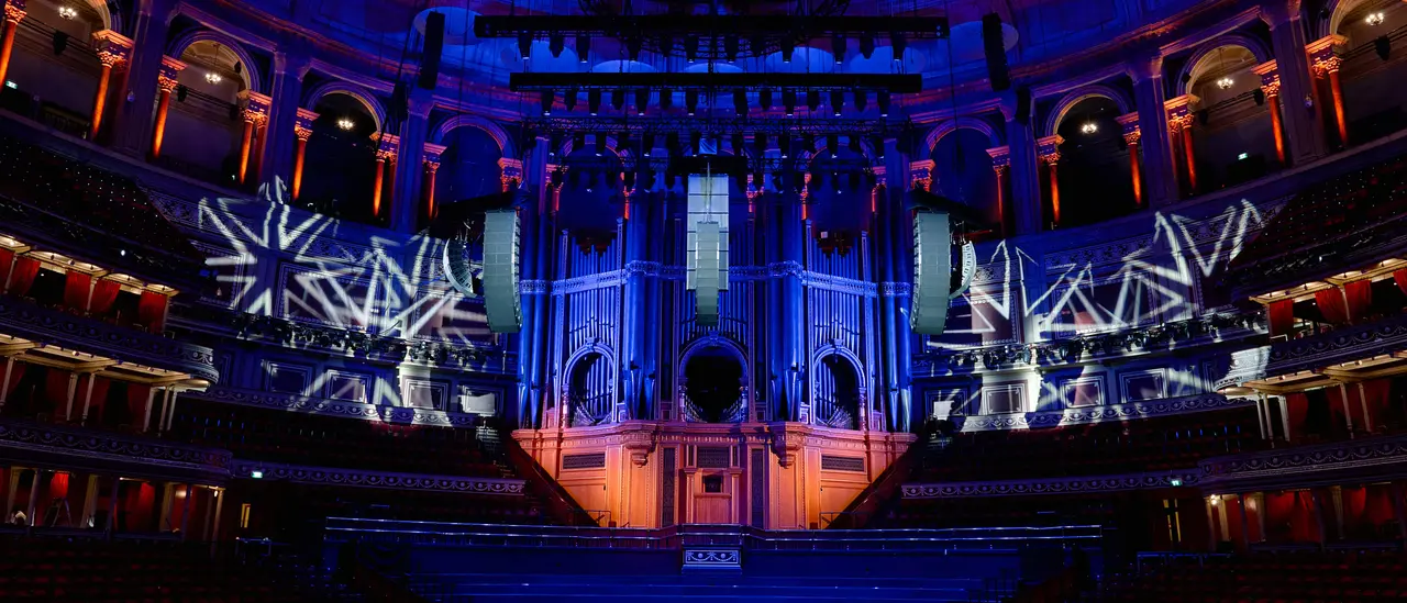 Concert hall interior featuring a large organ, illuminated with blue and orange lighting, and decorative projections on the walls.