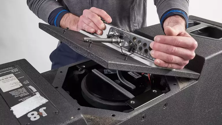 A person is opening the lid of a speaker cabinet, revealing internal components and wiring.