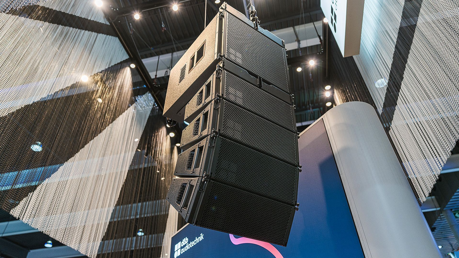 A large, suspended sound speaker system is displayed in a modern exhibition space, showcasing its design and technology.
