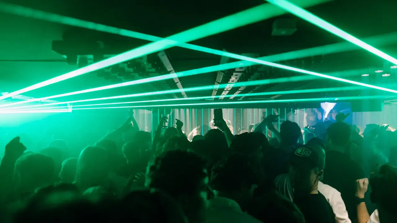 Crowd dancing in a dimly lit venue with green laser lights creating dynamic patterns overhead.