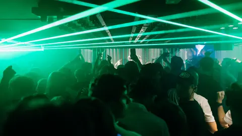 Crowd dancing in a dimly lit venue with green laser lights creating dynamic patterns overhead.