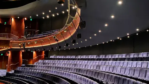 Empty theater interior featuring rows of plush seats and a curved balcony with overhead lighting.
