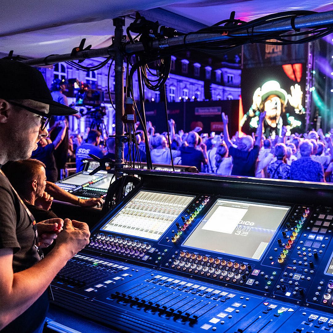 Sound engineer operating a mixing console in front of a live concert crowd, with colorful stage lights illuminating the performance.