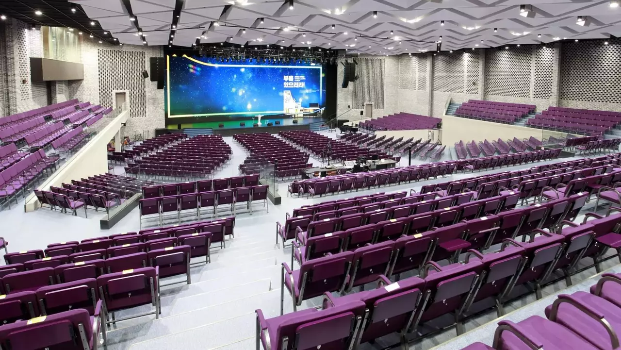 A spacious auditorium featuring rows of purple seats, a large stage with a screen, and modern architectural design elements.
