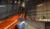 View of a theater interior showing rows of orange seats and overhead rigging with lighting equipment and structural elements.