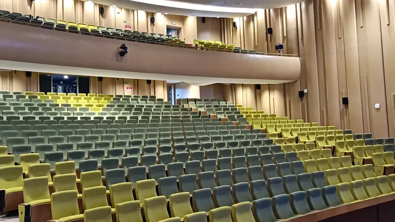 Empty auditorium with tiered seating in green and yellow, featuring a modern design and soft lighting.
