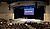 Empty auditorium with tiered seating facing a stage, featuring a large screen displaying "THE AUSTIN STONE."