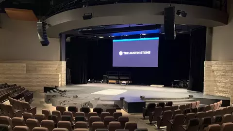 Empty auditorium with tiered seating facing a stage, featuring a large screen displaying "THE AUSTIN STONE."