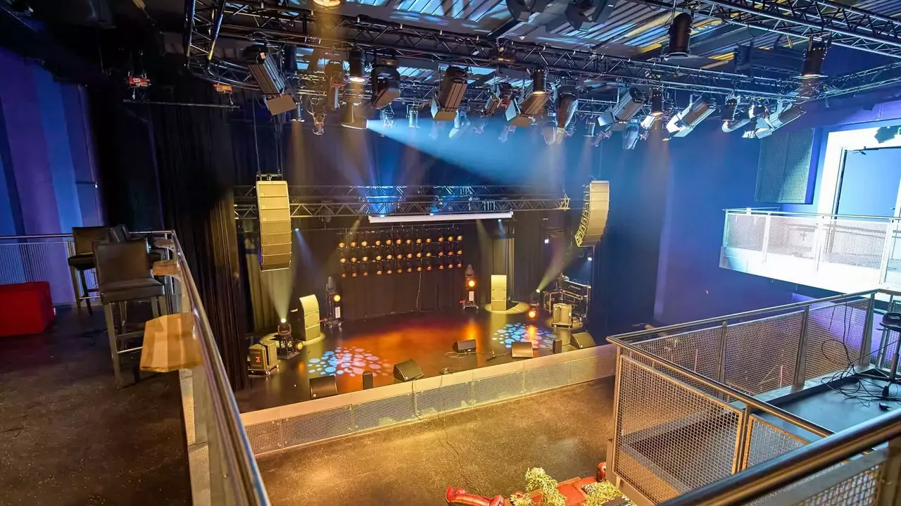 A concert stage with lighting and sound equipment, viewed from an upper level, featuring seating areas and a darkened performance space.