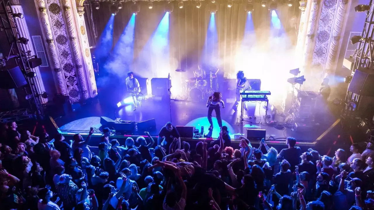 A lively concert scene with a band performing on stage, surrounded by an enthusiastic crowd with raised hands and colorful stage lighting.