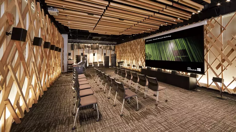 Modern conference room featuring rows of chairs, wooden wall accents, and a large screen displaying green graphics.