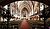 Interior of a church featuring a long aisle, wooden pews, ornate chandeliers, and a stained glass window at the altar.