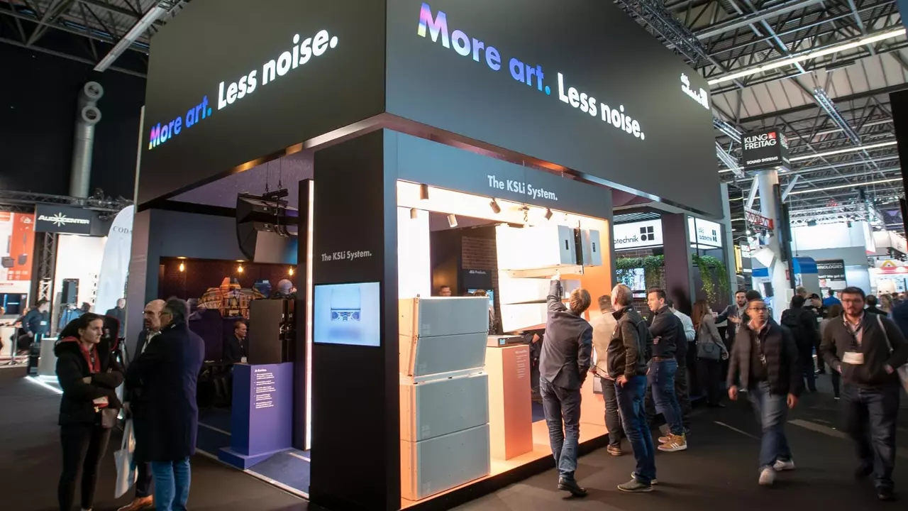 Exhibition booth featuring the slogan "More art. Less noise." with visitors interacting and viewing the KSL system displays.