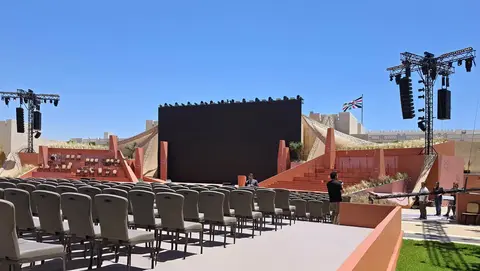 A large screen displays the Jordanian flag at an outdoor event, with a crowd seated in front and audio equipment in the foreground.