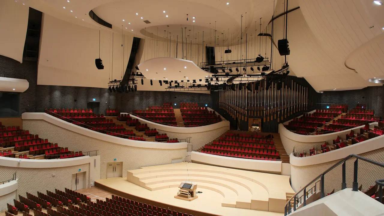Concert hall interior featuring tiered seating, a central stage, and a large pipe organ, with modern architectural design elements.