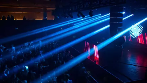 A crowd enjoys a live performance under vibrant blue and red stage lights, creating an energetic atmosphere in a dimly lit venue.
