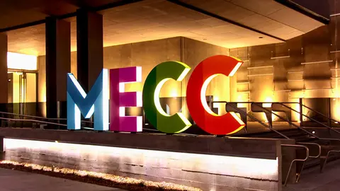 Colorful letters spelling "MECC" are displayed prominently outside a building, illuminated by warm lighting.