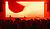 Crowd at a concert with silhouetted performers in front of a large red screen displaying abstract visuals.