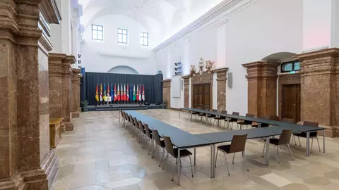 A large conference room featuring a long table with chairs, decorated with various national flags in the background.