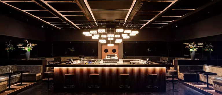 Modern bar interior featuring a sleek counter, stylish seating, and decorative lighting, creating an elegant atmosphere.