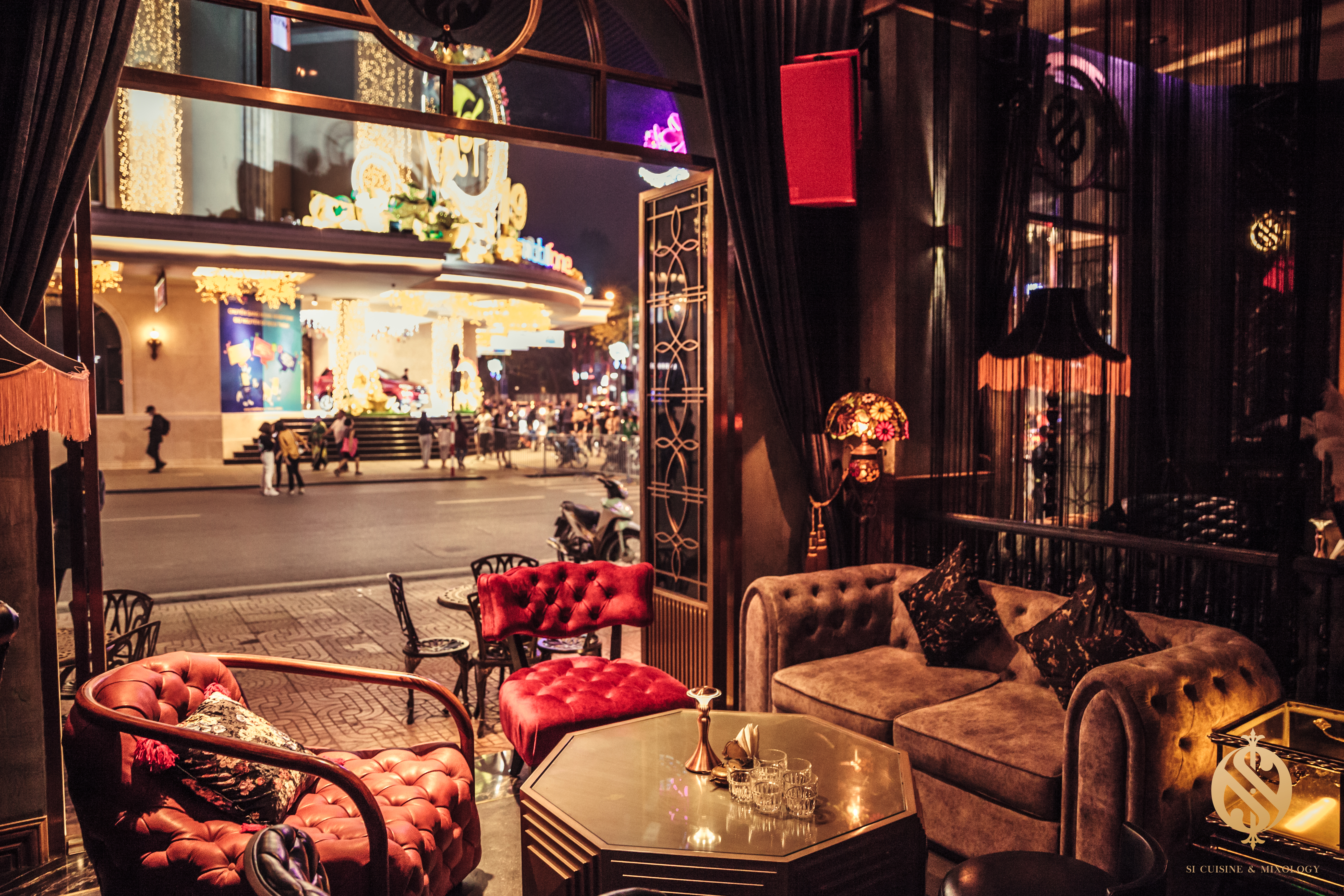 Luxurious lounge with plush seating and a decorative table, overlooking a bustling street illuminated by bright lights.